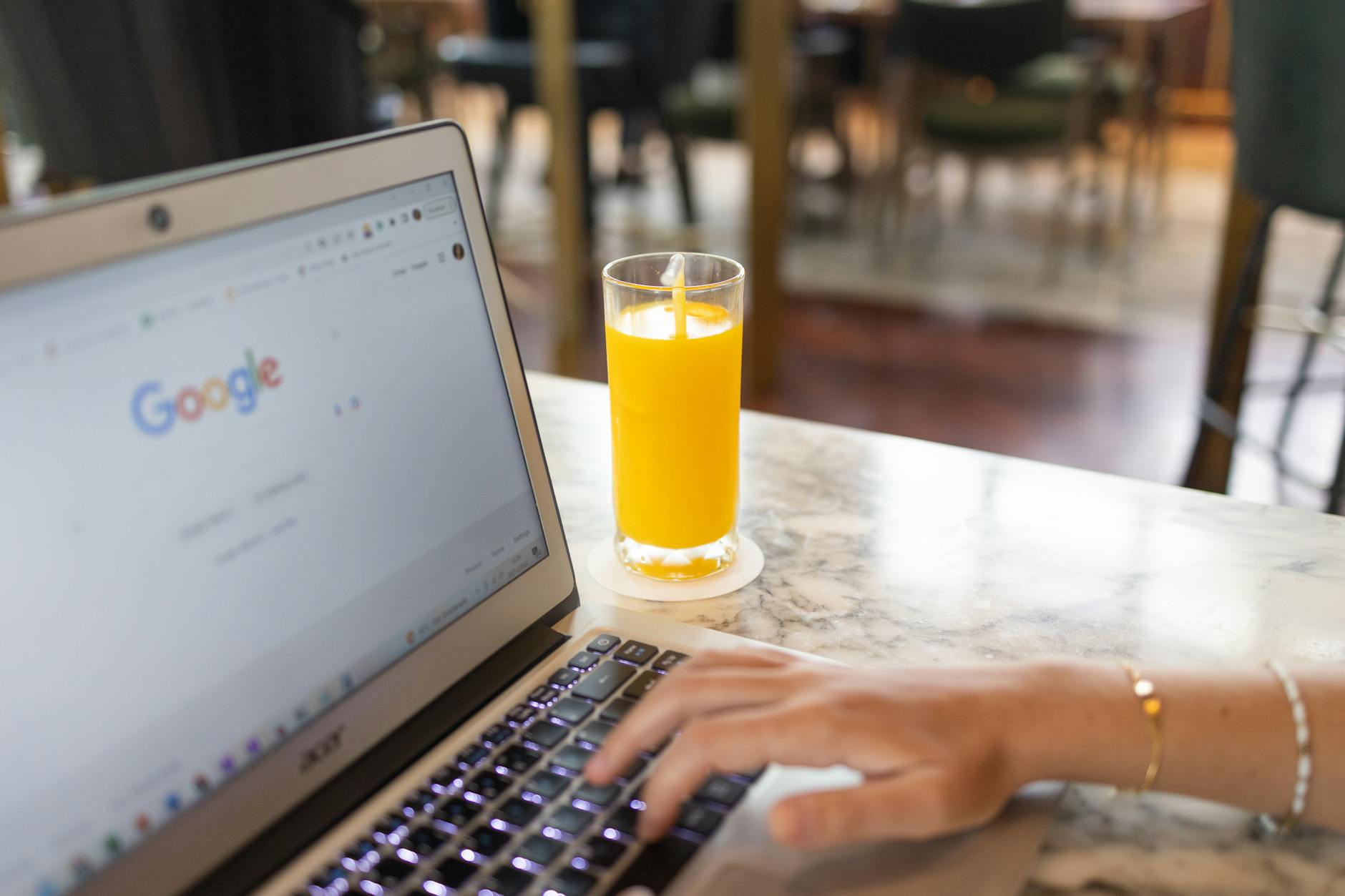A laptop with a Google search page and a glass of orange juice