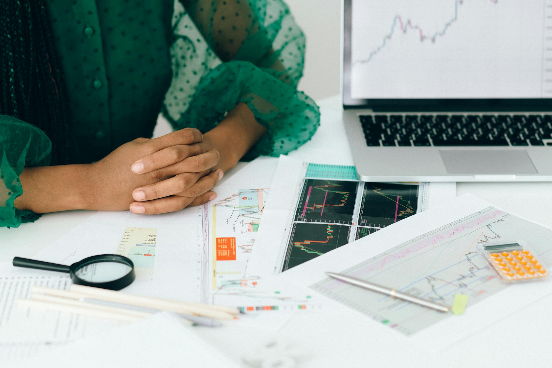 Hands resting on a table with financial charts and a laptop