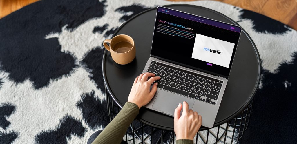 A person using a laptop on a coffee table with a cup nearby
